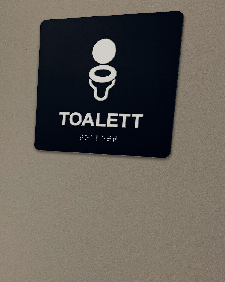 Taktil skylt med text Toalett och blindskrift